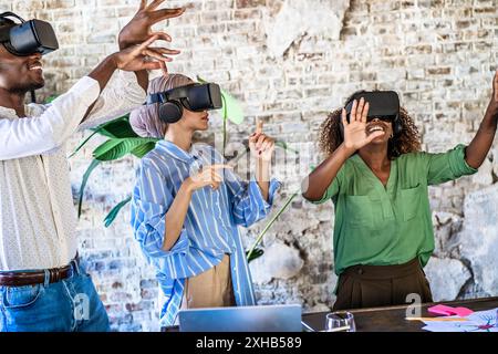 Gruppo multiculturale che utilizza i visori VR in un ufficio contemporaneo. Professionisti diversi che sperimentano una tecnologia immersiva, che mette in mostra innovazione e tè Foto Stock