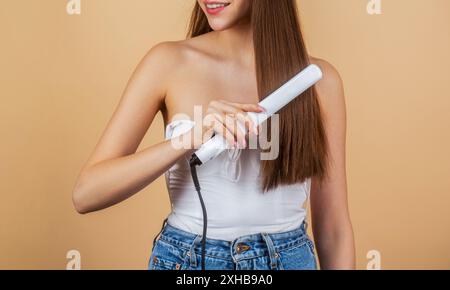 Ragazza che tiene i ferri da stiro. Acconciatura. Parrucchiere. Ferri per lisciare i capelli. Acconciatura. Bella donna sorridente che stirava capelli lunghi con capelli piatti Foto Stock