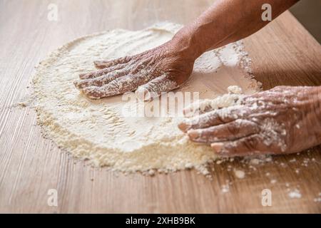 Impastare su un tavolo coperto di polvere bianca. Farina a mano. Affina il fornaio con la farina in cucina. Mani donna ricoperta di farine. Le mani delle donne, la farina e l'impasto Foto Stock