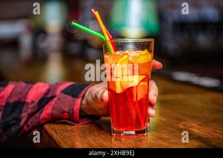 Tenere a mano il bicchiere del cacciavite cocktail con il tubo su uno sfondo luminoso. Concept party, relax, alcol. Uomo che regge un bicchiere di cocktail negroni Foto Stock