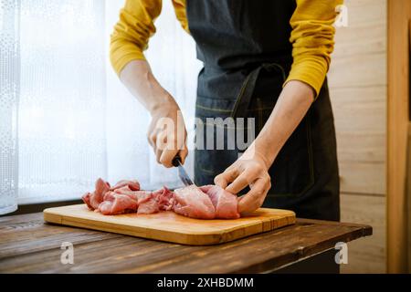 L'uomo irriconoscibile taglia la carne di maiale in pezzi grandi in cucina Foto Stock