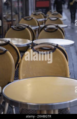Francia, Parigi - 05 gennaio 2024 - fila di sedie in legno e tavoli in acciaio fuori da un caffè in strada nella città di Parigi. Area salotto vuota all'aperto con Yell Foto Stock