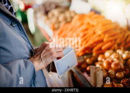 Una donna anziana con la mano nel portafoglio, che si prepara a pagare i prodotti in un mercato. Foto Stock