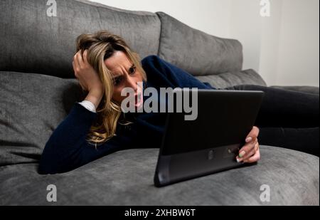 Donna con espressione facciale sorpresa che guarda cattive notizie su tablet. Emozioni negative, espressioni facciali umane Foto Stock