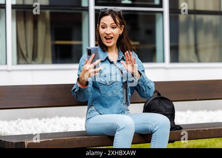Una donna siede su una panchina mentre usa il suo smartphone. Foto Stock