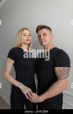 Bella coppia di moda donna e uomo in un elegante modello di t-shirt nera in piedi su uno sfondo bianco nella stanza Foto Stock