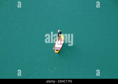 Uomo con cappello in paddleboard (SUP) sulle acque verdi Foto Stock