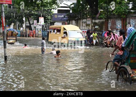 Persone e veicoli che cercano di muoversi attraverso la strada bagnata di Dacca, Bangladesh, il 26 luglio 2024 Foto Stock
