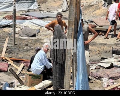 Khan Younis, Gaza. 13 luglio 2024. I palestinesi osservano i detriti delle tende distrutte e realizzano strutture abitative a turni a seguito di uno sciopero militare israeliano sul campo di al-Mawasi per sfollati interni (IDP), vicino alla città di Khan Yunis, nella parte meridionale della Striscia di Gaza, sabato 13 luglio 2024, in cui sono state uccise 71 persone. Al-Mawasi era stata dichiarata zona sicura da Israele. Foto di Saber Arar/UPI credito: UPI/Alamy Live News Foto Stock