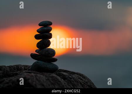 Un piccolo cairn posto su una roccia al tramonto con il sole che tramonta sullo sfondo Foto Stock