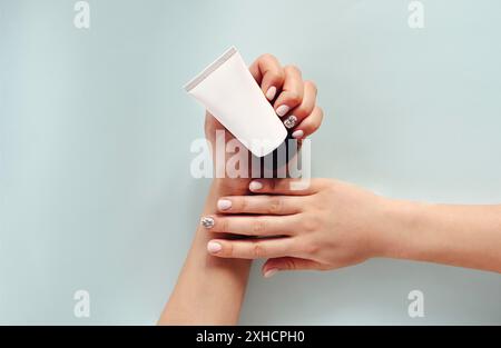 Vista dall'alto di una donna anonima con mani curate che mostra un tubo bianco di crema su sfondo azzurro Foto Stock