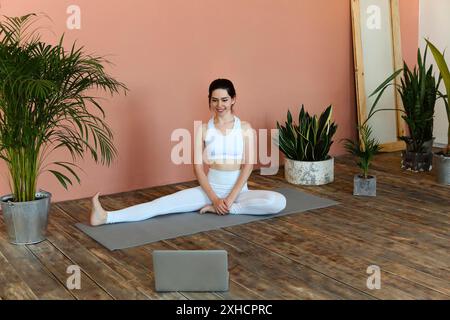 Content femminile in sportswear seduta su tappetino e gambe stretching prima di esercizi di yoga mentre si guarda tutorial online su computer portatile Foto Stock