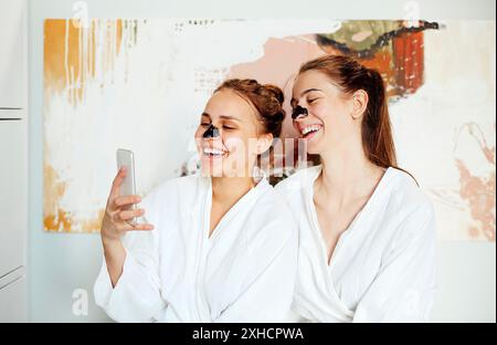 Compagnia di adorate amiche in accappatoi e con occhielli che prendono selfie sullo smartphone mentre si rilassano nel centro termale durante il fine settimana Foto Stock