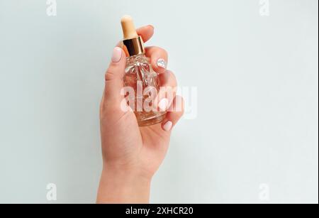 Vista dall'alto di una donna anonima con mani curate che mostrano un vuoto bottiglia di olio essenziale su fondo azzurro Foto Stock