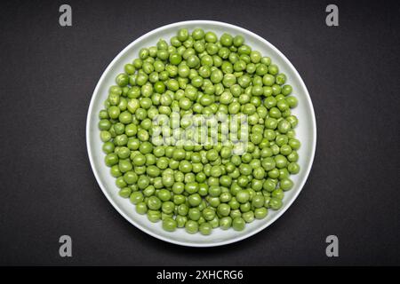 Vista dall'alto di un piatto con piselli verdi freschi isolati su sfondo nero. Pisum sativum Foto Stock