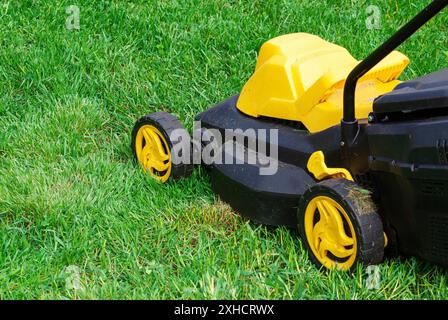 Primo piano della macchina rasaerba elettrica che lavora su erba verde Foto Stock