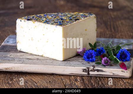 Formaggio di montagna con fiori su legno Foto Stock