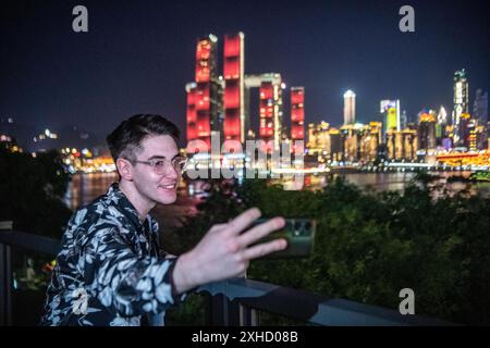 (240713) -- CHONGQING, 13 luglio 2024 (Xinhua) -- Ilia Anfilatov prende i video della vista notturna della città a Nanbin Road, nella municipalità di Chongqing, nel sud-ovest della Cina, 12 luglio 2024. Gli studenti internazionali Ilia Anfilatov dalla Russia e Syyra Alee dal Pakistan studiano alla Southwest University di Chongqing da oltre un anno. Nel loro tempo libero, amano passeggiare per la città e condividere le loro esperienze sui social media. Grazie alla loro condivisione, molti dei loro amici e famiglie sono attratti dallo splendido paesaggio e dalla diversa cultura della Cina e hanno in programma di imbarcarsi in un viaggio a chi Foto Stock