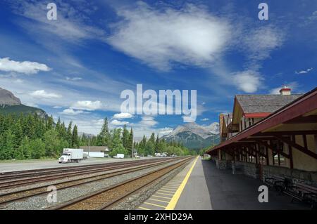 Binari ferroviari accanto a una stazione con paesaggio montano e cielo nuvoloso sullo sfondo, Banff, Montagne Rocciose, Alberta, Canada Foto Stock