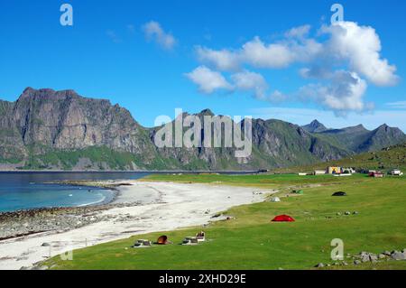 Paesaggio costiero con spiaggia e campeggi su prato verde, con montagne e cielo azzurro, Utakleiva, vestavagoya, Nordland, Lofoten, Norvegia Foto Stock