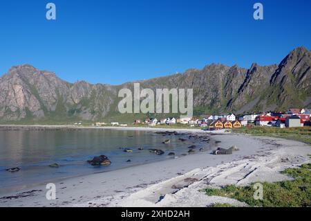 Pittoresco villaggio costiero con case colorate circondato da alte montagne e mare calmo, Bleik, Vesteralen, Langoya, Nordland, Norvegia Foto Stock