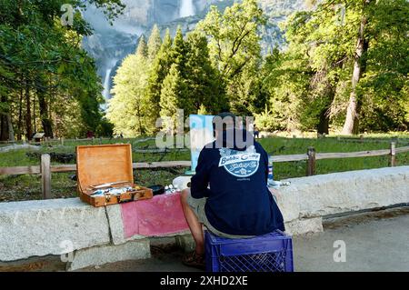 Un artista seduto su una cassa di plastica dipinge un paesaggio in una giornata di sole nel Parco Nazionale di Yosemite, California, USA Foto Stock