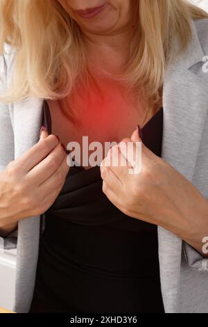 Menopausa. La donna soffia aria su se stessa per raffreddarsi durante il flash caldo al tavolo in cucina Foto Stock