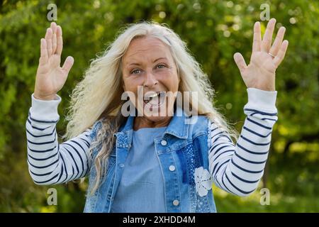 Una donna anziana alza le braccia e goditi la bella giornata Foto Stock