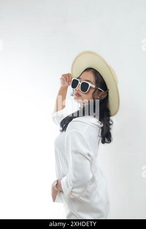 Ritratto di una bella giovane donna asiatica in abiti bianchi casual con cappello di paglia e occhiali da sole isolati su sfondo bianco. Concetto di vacanza estiva Foto Stock