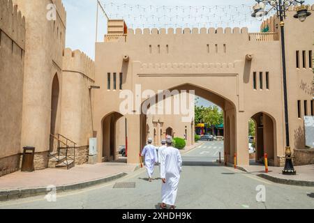 Tradizionalmente vestite di tobe bianche che camminano attraverso la porta dell'acida fortezza araba, Nizwa, sultanato dell'Oman Foto Stock