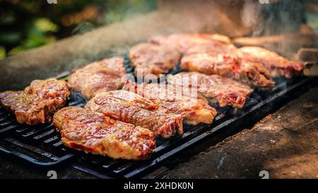 Primo piano di un grill con più bistecche sfrigolanti sulle griglie, fumo che fuoriesce dalla carne. Foto Stock