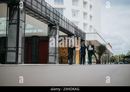 Tre professionisti che camminano e discutono all'esterno di un edificio moderno Foto Stock