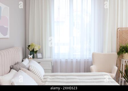 Letto grande, cassettiera, poltrona e finestra con tende nella camera da letto. Design degli interni Foto Stock