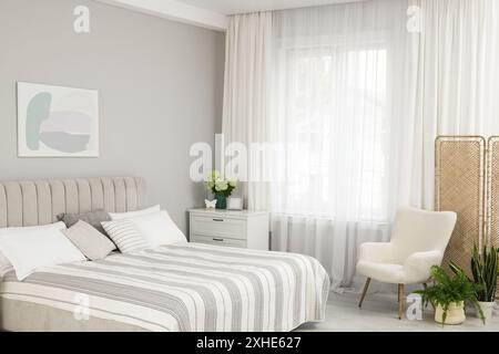 Letto grande, cassettiera, poltrona e finestra con tende nella camera da letto. Design degli interni Foto Stock