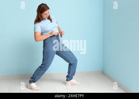 Donna sovrappeso in jeans stretti su sfondo blu. Concetto di peso eccessivo Foto Stock