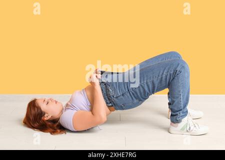 Donna sovrappeso in jeans stretti su sfondo giallo. Concetto di peso eccessivo Foto Stock