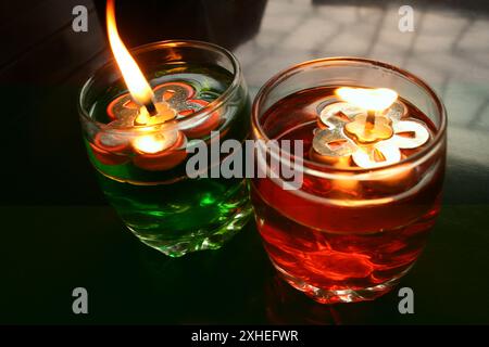 Illuminazione dalla fiamma di candele decorative colorate in bicchieri posti sul tavolo. Foto Stock
