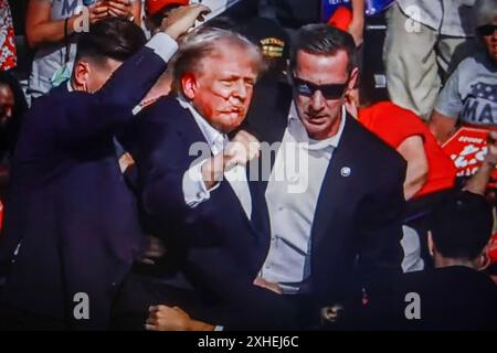 In questa illustrazione fotografica, uno schermo mostra l'ex presidente degli Stati Uniti Donald Trump girato all'orecchio durante una manifestazione che stava tenendo a Butler. L'ex presidente degli Stati Uniti Donald Trump è stato ferito in una sparatoria a un raduno che stava tenendo a Butler, Pennsylvania, nell'ambito della sua campagna elettorale in vista delle elezioni presidenziali statunitensi del 2024. Secondo gli ultimi rapporti, agenti segreti hanno ucciso un assassino e un partecipante al rally è morto per mano dello stesso assassino, la sparatoria al rally è stata indagata come un tentato omicidio dell'ex presidente Trump, la Associated Press riferisce che citava il Butler Foto Stock