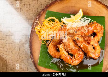 Gamberi fritti in profondità con salsa tamarinda su foglia di banana e piatto di legno con uova a fette, spaghetti fritti e lime. Foto Stock
