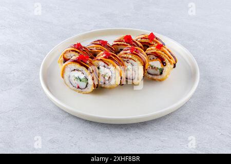 Sushi roll caldo con surimi, cetrioli e formaggio spalmabile, versato con salse piccanti e unagi, guarnito con caviale masago Foto Stock
