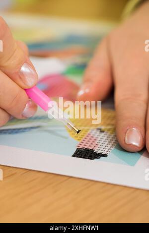 Primo piano di una mano che posiziona cristalli su una tela per un progetto di pittura a diamanti. Mosaico diamantato Foto Stock