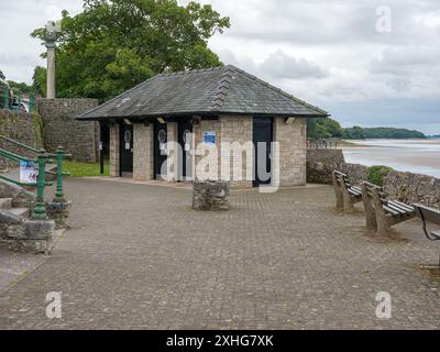 Arnside Cumbria Regno Unito 13/07/2024. Un piccolo bagno pubblico in pietra vicino ad una passeggiata sul mare con panche e ringhiere verdi in una giornata nuvolosa. Foto Stock