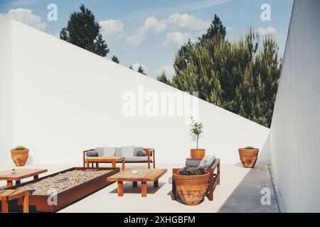 Moderno patio esterno con mobili in legno che includono panche e tavoli, disposto intorno a un caminetto in pietra. Piantatrici di terracotta con vegetazione e Foto Stock