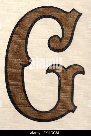 Antica lettera maiuscola decorativa G in oro con contorno nero su sfondo crema. Foto Stock