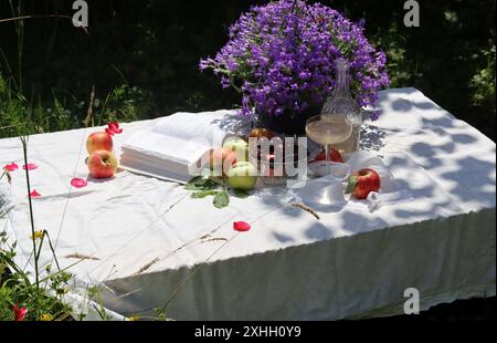 Picnic estivo in giardino su una tovaglia bianca con frutta fresca, fiori e champagne. Giornata calda in un giardino. Cena romantica a tavola. Foto Stock