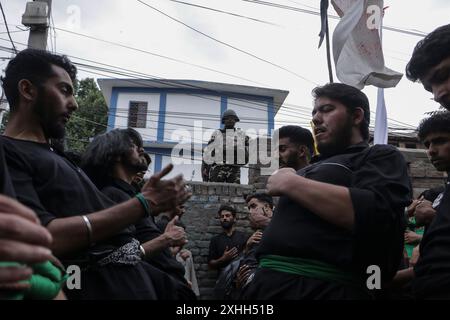 14 luglio 2024, Srinagar, Jammu e Kashmir, India: un personale armato indiano fa la guardia mentre i musulmani sciiti Kashmiri picchiavano il loro petto a Nohay (lamentazioni) mentre partecipavano a una processione di Muharram durante il "lutto di Muharram" rispetto religioso il settimo giorno di Muharram, il primo mese del calendario islamico, a Srinagar. Il settimo di Muharram è osservato e commemorato come il giorno in cui le forniture d'acqua dell'Imam Hussain a.S e dei suoi compagni si sono essiccate. (Immagine di credito: © Adil Abass/ZUMA Press Wire) SOLO PER USO EDITORIALE! Non per USO commerciale! Foto Stock