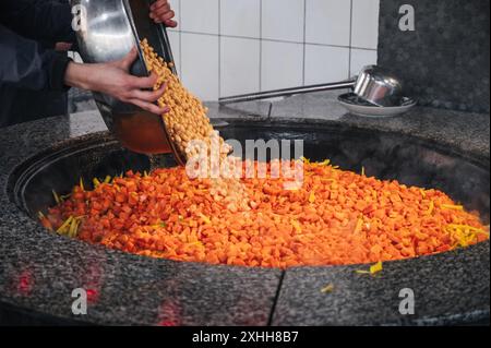 Lo chef maschile aggiunge ceci a un calderone con carote per cucinare il tradizionale pilaf uzbeko orientale nella cucina asiatica di un ristorante in Uzbekistan Foto Stock