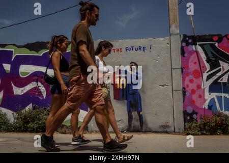 Barcellona, Spagna. 14 giugno 2024. I pendolari passano davanti a un murale dell'artista urbano italiano "TVBoy", Salvatore Benintende. Intitolato "il futuro", i graffiti raffigurano Lionel messi in possesso di una maglia del FC Barcelona con il suo ex numero 10 e il nome Lamine Yamal, presentando la giovane stella il giorno in cui potrebbe diventare il più giovane vincitore di un campionato europeo di UEFA, come suo successore. Crediti: Matthias Oesterle/Alamy Live News Foto Stock