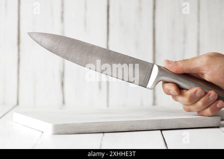 Tenendo in mano il coltello chef in acciaio fuso sul tagliere, un coltello da cucina moderno e affilato Foto Stock