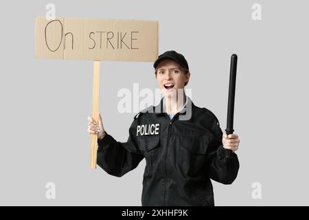 Protesta contro un agente di polizia che tiene in mano il bastone e un cartello con il testo SULLO SCIOPERO su sfondo grigio Foto Stock